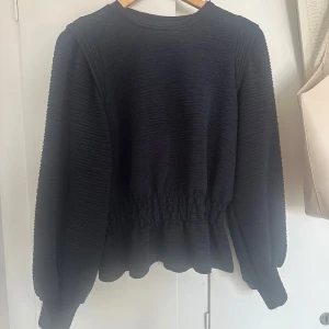Svart långärmad topp från Pieces - Säljer en svart långärmad topp från Pieces med strukturerat tyg och markerad midja. Tröjan har rund halsringning och ballongärmar som ger en snygg siluett. Jätte fint skick och inte använd så mycket, max 3 gånger! Skriv vid intresse eller funderingar❤️