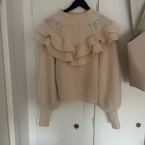 Beige stickad tröja med volang - Superfin beige stickad tröja med breda volangdetaljer över axlarna och ribbad struktur. Tröjan har lång ärm och en mysig, och är i ett jätte fint skick! Skriv vid intresse eller funderinger!🙏