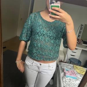 Grön spetsblus från Lindex - Säljer en grön blus från Lindex i spetsmaterial. Blusen har korta ärmar och ett blommigt mönster. Den är något croppad och har rund halsringning. Perfekt för dig som vill ha en luftig och snygg topp till sommaren!