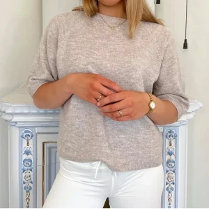 Beige stickad tröja med kort ärm - Mysig beige stickad tröja med rund hals och korta ärmar. Perfekt för lager-på-lager och passar till både jeans och kjol. Enkel och stilren design som är lätt att matcha. Väldigt fint skick 