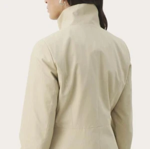 Beige vårkappa från Part Two - Snygg beige vårkappa från Part Two med guldfärgade dragkedjor och hög krage vid heldraget upp som viksned vid neddraget. Jackan har lång ärm och rak passform. Perfekt för våren och stilrena outfits. Går och matcha med nästan allt! Helt nytt skick och danskt design märke! Nypris=1400kr.