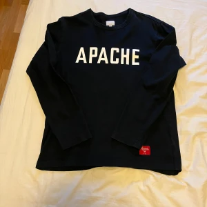 Supreme apache lång ärmad tröja/ kofta - Säljer en svart långärmad tröja från Supreme i 100% bomull med vit text 'APACHE' på bröstet. Klassisk rund halsringning och diskret Supreme-märke nertill. Perfekt för dig som gillar streetwear och enkel stil. Fint skick i storlek M.