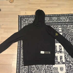 Svart hoodie från Stone Island - Säljer en svart hoodie från Stone Island med klassisk logotyp-patch på vänster ärm. Tröjan har huva och en stor magficka framtill. Säljer den då den är lite för liten för mig. Original pris på tröjan är 3300kr och är köpt på Jupiter i Stockholm. Kvitto finns, och tröjan är köpt i februari.