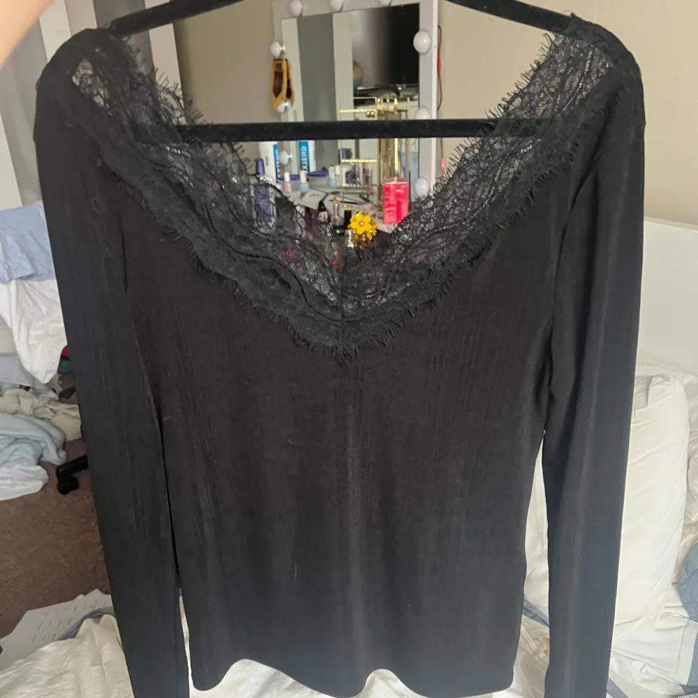Säljer en svart långärmad topp med v-ringning och fina spetsdetaljer längs halsringningen. Perfekt att styla till olika outfits och ger en elegant touch.. Yläosat.