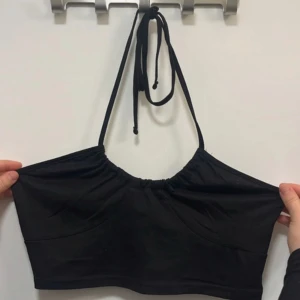 Svart croppad halterneck-topp - Säljer en svart croppad halterneck-topp med knyt i nacken. Enkel och stilren design, perfekt till sommaren. Tunt och stretchigt material som sitter snyggt på kroppen.