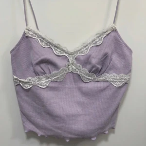 Ljuslila ribbad linnetopp med spets - Säljer en söt ljuslila ribbad linnetopp med tunna axelband och vit spetsdetalj längs bysten. Toppen har en croppad passform och vågig kant nertill. Perfekt för sommaren!
