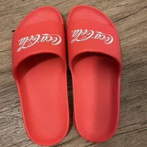 Röda Coca-Cola sandaler - Säljer ett par röda sandaler med Coca-Cola-logga på ovandelen. 