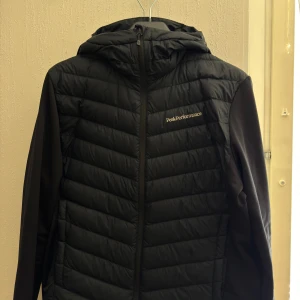 Svart hybridjacka från Peak Performance - Säljer en svart pufferjacka från Peak Performance med huva och dragkedja. Jackan är pefekt till svensk väder och till träning. Säljs pga att den inte passar mig Storlek M. Nypriset är 2700. Pris kan diskuteras