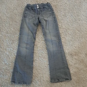 Grå jeansbyxor, bootcut, från Gina Tricot - Säljer ett par grå jeansbyxor från Gina Tricot i storlek 152. Byxorna har raka ben, två framfickor och två bakfickor samt stängs med två knappar och en dragkedja. Bootcut jeans.