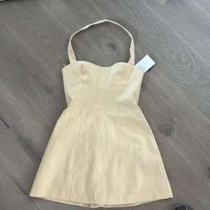 Ljusgul kort klänning från Zara - Supersöt ljusgul kort klänning från Zara med markerad byst, breda axelband och figurnära passform. Klänningen har en slät yta och är fodrad inuti för extra komfort. Perfekt för dig som vill sticka ut med en stilren och trendig look.