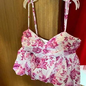 Blommig vit och rosa linnetopp från Zara  - Supersöt linnetopp med tunna axelband och volangig nederdel. Toppen är vit med rosa blommigt mönster. Helt oanvänd, ändast provad men var för liten! 