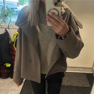 Beige skepparkavaj med bred krage - Snygg beige kappa med bred krage och dubbelknäppning. Jackan har en loose passform och är tillverkad i ett mjukt material som känns lyxigt. Perfekt för dig som vill ha en stilren och trendig look i höst och vinter.