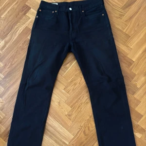 Svarta Levi's 501 jeans. ENDAST TESTADE! Köpta för 1149kr - Klassiska svarta Levi's 501 jeans med raka ben och femficksdesign. Byxorna har knappgylf och den ikoniska läderpatchen bak i midjan. Perfekta för dig som gillar tidlös stil och vill ha ett par jeans som funkar till allt.