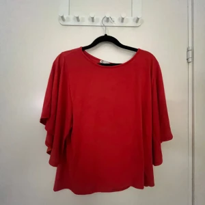 Röd topp med vida ärmar - Säljer en röd topp med rund halsringning och vida, trekvartsärmar. Toppen har en lös passform och är perfekt för dig som gillar en enkel men ändå statement look.