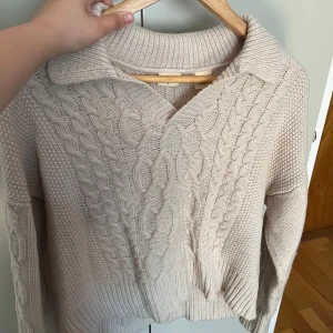 Beige stickad tröja med krage från Levi's - Säljer en beige stickad tröja från Levi's i storlek S. Tröjan har kabelstickat mönster framtill, krage och långa ärmar. Perfekt för lager-på-lager och en mysig vardagslook.