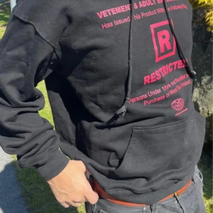 Vetements 18+ Rated R Restricted Adult Entertainment Hoodie - Säljer en svart hoodie från Vetements med rött tryck både fram och bak. På framsidan står det 'RESTRICTED' och på baksidan finns en stor grafisk logga och texten 'ADULT ENTERTAINMENT'. Hoodien har magficka och dragsko i huvan.