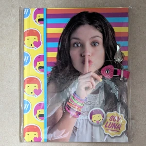 Soy Luna Dagbok med Lås - Färgglad dagbok inspirerad av Soy Luna, perfekt för dig som vill skriva ner dina hemligheter! Dagboken har ett lås och nyckel för extra säkerhet. Omslaget pryds av Luna och coola emojis – perfekt för fans av serien och dig som gillar att uttrycka dig kreativt. Dagboken är fortfarande i original plast förpackning 