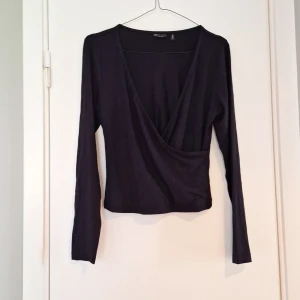 Svart omlottopp från ASOS Design - Svart långärmad omlottopp från ASOS Design. Topp med djup v-ringning och croppad passform, perfekt att styla med höga jeans eller kjol. Mjuk och stretchig känsla, enkel men ändå snygg detalj till din outfit. Oanvänd.