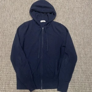 Mörkblå hoodie i kashmir från Soft Goat - Mysig mörkblå hoodie från Soft Goat i mjuk kashmir. Tröjan har dragkedja framtill, huva med dragsko och långa ärmar. Perfekt för en avslappnad och stilren look.