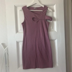 Ljuslila tight klänning med cut-out detalj - Säljer en ljuslila tight klänning med unik cut-out och asymmetrisk axel. Klänningen är ärmlös och har en modern, stilren look som passar perfekt för dig som vill sticka ut.