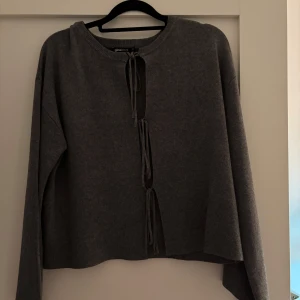 Grå stickad kofta från Gina Tricot - Säljer en grå stickad kofta från Gina Tricot i storlek XS. Koftan har långa ärmar och knytning framtill med tre knytband. Perfekt för lager-på-lager och enkel att styla till olika outfits. Använd få gånger!