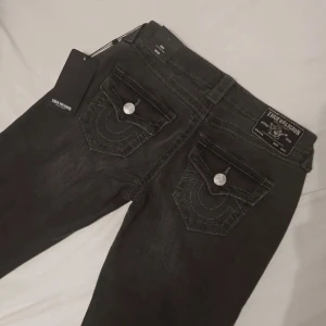 Mörkgråa bootcut jeans från True Religion - Säljer ett par super snygga mörkgråa lågmidjade bootcut jeans från True Religion. Jätte snygga! Säljer pga jag har för mycket jeans 🥲💕Strl:  W25☺️ Ursprungligt pris: 1300kr