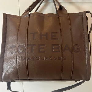  Tote Bag - Säljer en brun Tote Bag. Väskan har en präglad logga framtill och rejäla handtag. Perfekt storlek för att få plats med allt du behöver och en stilren design som sticker ut.
