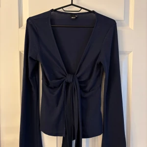 Mörkblå omlottopp från Gina Tricot - Snygg mörkblå omlottopp från Gina Tricot med lång ärm och djup v-ringning. Toppen har fått lite små hål pga att jag har använt en ”nopp maskin”