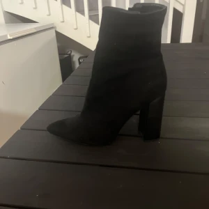 Svarta mocka boots med klack - Säljer ett par svarta boots i mocka med hög klack och rund tå. Skorna har en stilren och enkel design som passar till många olika outfits. Perfekta för dig som vill ha ett par klassiska boots med lite höjd.