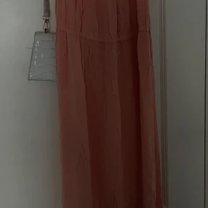 Ljusrosa långklänning med kort ärm - Säljer en luftig och lång ljusrosa klänning med korta ärmar. Klänningen har en avslappnad passform och är perfekt för varma dagar. Materialet känns lätt och flowy, vilket ger en skön känsla.