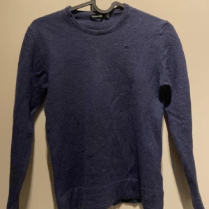 Mörkblå stickad tröja från J. Lindeberg - Säljer en mörkblå stickad tröja från J. Lindeberg med diskret broderad logga på bröstet. Tröjan har rund halsringning och långa ärmar, perfekt för lager-på-lager under kyliga dagar. Enkel och stilren design som funkar till det mesta.