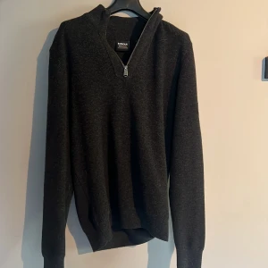Mörkgrå stickad tröja med dragkedja från Barbour International - Säljer en mörkgrå/svart stickad tröja från Barbour International med halv dragkedja framtill. Använd 1-2 gånger som ny! Nytt pris 1299. Vårt pris 600!