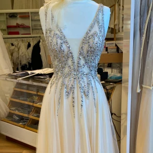 Champagnefärgad långklänning med glittriga detaljer - Säljer min älskade balklänning❤️☹️ Den är champagnefärgad med djup v-ringning och glittriga paljettdetaljer upptill. Klänningen har ärmlös design, markerad midja och ett flytande, lätt tyg i kjolen. Den är sydd för 163 cm så att klackarna syns lite grann i botten. Köpt på Rafaela Mode i Norrköping. Tror det endast finns en i sverige. Köptes för 8000 kronor och är endast använd 1 gång.