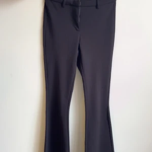 Svarta bootcut kostymbyxor - Snygga svarta kostymbyxor med bootcut-snitt och klassiska bälteshällor. Byxorna har en stilren look och är perfekta för dig som gillar en tidlös och clean stil. Materialet känns mjukt och följsamt.