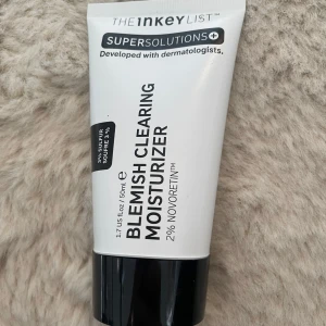 The Inkey List Blemish Clearing Moisturizer - En vit och svart tub med Blemish Clearing Moisturizer från The Inkey List. Innehåller 3% svavel och 2% Novoretin, perfekt för dig som vill ha en återfuktande ansiktskräm som hjälper mot finnar. Tuben rymmer 50 ml och är enkel att ta med i väskan.