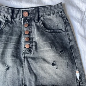 Grå jeanskjol från OneTeaspoon - Snygg grå kort jeanskjol från OneTeaspoon med slitna detaljer, knappar framtill och klassiska fickor. Rå och cool look med slitningar och tvättad finish. Perfekt för dig som gillar streetstyle och denim vibes. Har inte använt den. För de va för liten för mig. Köpte den för 800kr