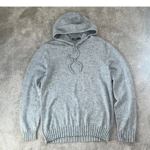 Grå stickad hoodie från Dressmann - Säljer en grå stickad hoodie från Dressmann i storlek L. Tröjan har huva med dragsko och ribbade muddar vid ärmslut och nederkant. Perfekt för en avslappnad och stilren look.