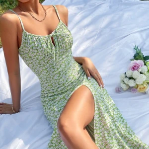 Grön blommig sommarklänning med slits - Söt grön klänning med vita blommor, smala axelband och en hög slits framtill. Klänningen har en figurnära passform upptill och faller mjukt nedåt. Perfekt för varma dagar och picknick i parken💕klänningen är nästintill oanvänd! 💕