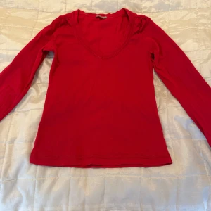 Röd v-ringad långärmad topp från Cue - Säljer en röd långärmad topp från Cue med v-ringning och lätt rynkade axlar. Tunn och mjuk i materialet, perfekt för lager-på-lager eller som den är. Enkel och stilren design som passar till mycket.