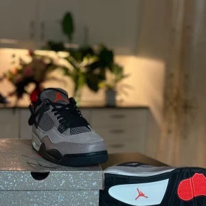 Nike Air Jordans 4 Taupe Haze - Säljer ett par Nike Air Jordans 4 Taupe Haze med grå mocka, svarta detaljer och röda accenter. Skorna har klassisk mesh på sidorna, svart snörning och en vit sula med synlig Air-enhet. Perfekta för dig som vill sticka ut med stilrena sneakers.