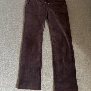 Bruna mjukisbyxor från Juicy Couture - Mysiga bruna mjukisbyxor från Juicy Couture med raka ben och stora fickor fram. Byxorna har resår i midjan och bakfickor med knapp. Perfekta för en avslappnad stil. Säljs i brist på användning (endast använd ett fåtal gångner)