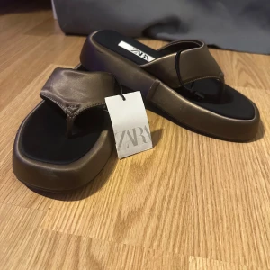 Bruna sandaler från Zara - Snygga bruna sandaler från Zara med en stilren design. De har en bred rem över foten och en fyrkantig tåform. Perfekta för en avslappnad sommarlook.