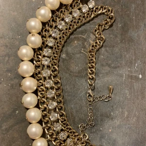 Halsband med pärlor och strass - Elegant halsband med stora vita pärlor och glittrande strassdetaljer. Kedjan är i guldton och justerbar för perfekt passform. Perfekt för att ge en lyxig touch till din outfit.