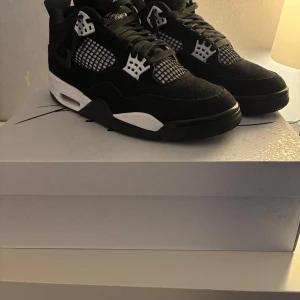 Air Jordans 4 retro White Thunder - Snygga svarta Nike Air Jordans med vita detaljer och klassisk snörning. Skorna har en ikonisk design med nätmönster på sidorna. Perfekta för dig som vill ha en stilren och sportig look. Kvitto och Lådan finns. Använd få gånger. Nypris 4299kr strl 43