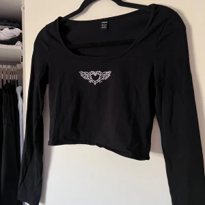 Svart långärmad topp med strass-detalj - Säljer en svart långärmad topp från Shein med ett glittrigt hjärtmönster framtill. Toppen har en rund halsringning och är tillverkad i ett mjukt material. Perfekt för en stilren look. Passar även bra till storlek S.   OBS! Har varit en body men jag har klippt av den och sytt den till en topp istället 🤗  Önskar du veta exakta mått? Tveka inte att höra av dig!