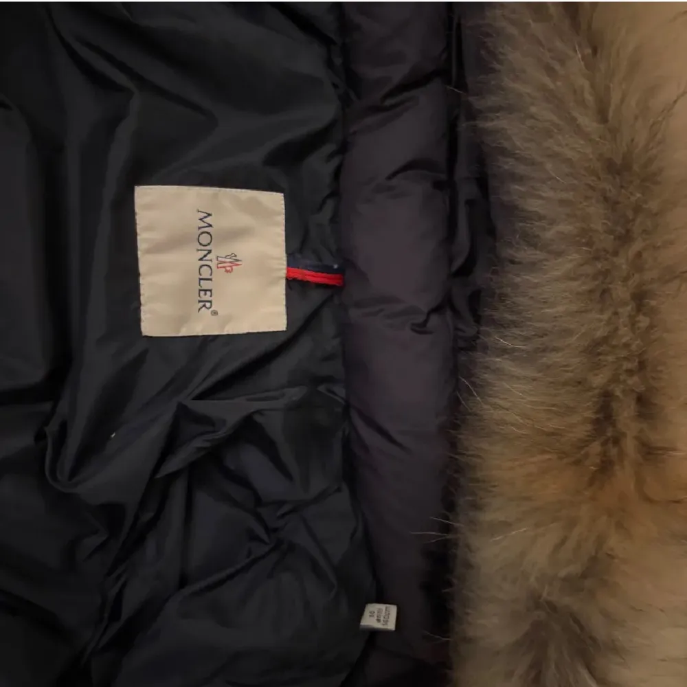 Säljer en snygg marinblå dunjacka från Moncler med pälshuva. Jackan har en dragkedja framtill och praktiska fickor med knappar. Perfekt för kalla dagar! Jackan saknar en knapp på luvan, därav det låga priset. Jackan är jätte fin med ,luva och utan luva.. Takit.