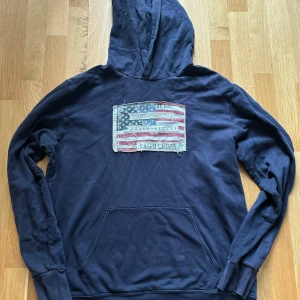Ralph Lauren - Denim supply  - Säljer en snygg mörkblå hoodie från Ralph Lauren med en stor amerikansk flagga på bröstet. Hoodien har en klassisk känguruficka och ribbade muddar vid ärmslut och nederkant. Perfekt för en avslappnad stil.