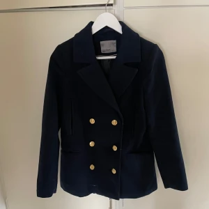 Mörkblå skepparkavaj från Vero Moda storlek XS - Snygg mörkblå skepparkavaj från Vero Moda med guldknappar i dubbelknäppt design. Jackan har en klassisk krage och långa ärmar, perfekt för en stilren look. Passar bra till både vardag och mer uppklädda tillfällen. Storleken är XS