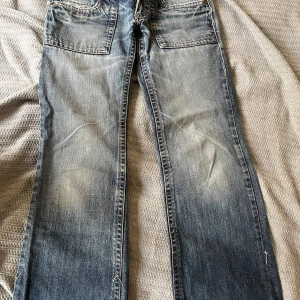 Blå jeansbyxor från craft  - Snygga blå lågmidjade bootcut jeans från craft med detaljer. Byxorna har en klassisk femficksdesign och en knappgylf. 17cm grenhöjd och 38 cm midjebredd. 2000tals stil.