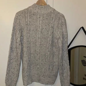 Grå stickad från Grunt  - Säljer en mysig grå stickad tröja med dragkedja. Perfekt för kyliga dagar med sitt klassiska mönster och långa ärmar. Passar bra till både jeans och chinos. Det står storlek XXL men den sitter som M.